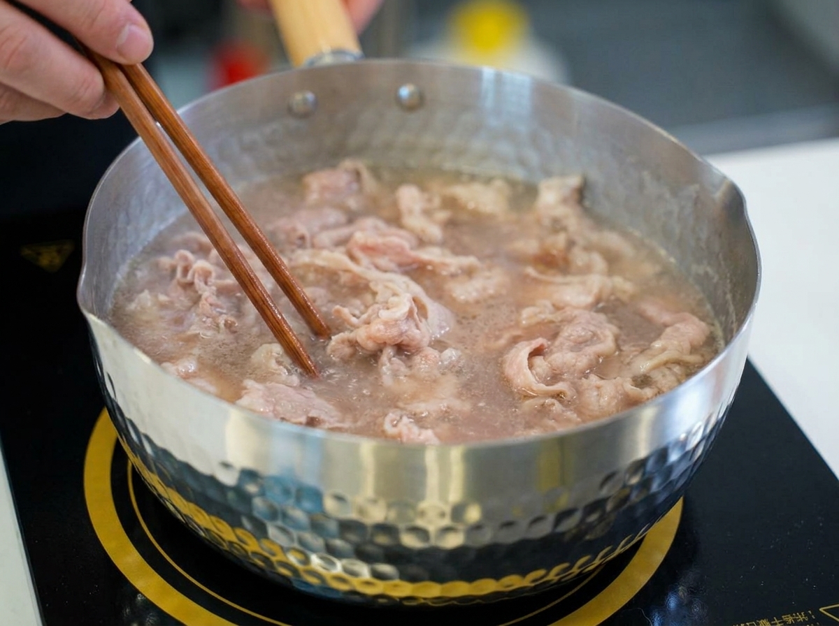 De fines tranches de bœuf remuées avec des baguettes en bois dans une casserole deau frémissante alors quelles passent du rose cru au brun clair.