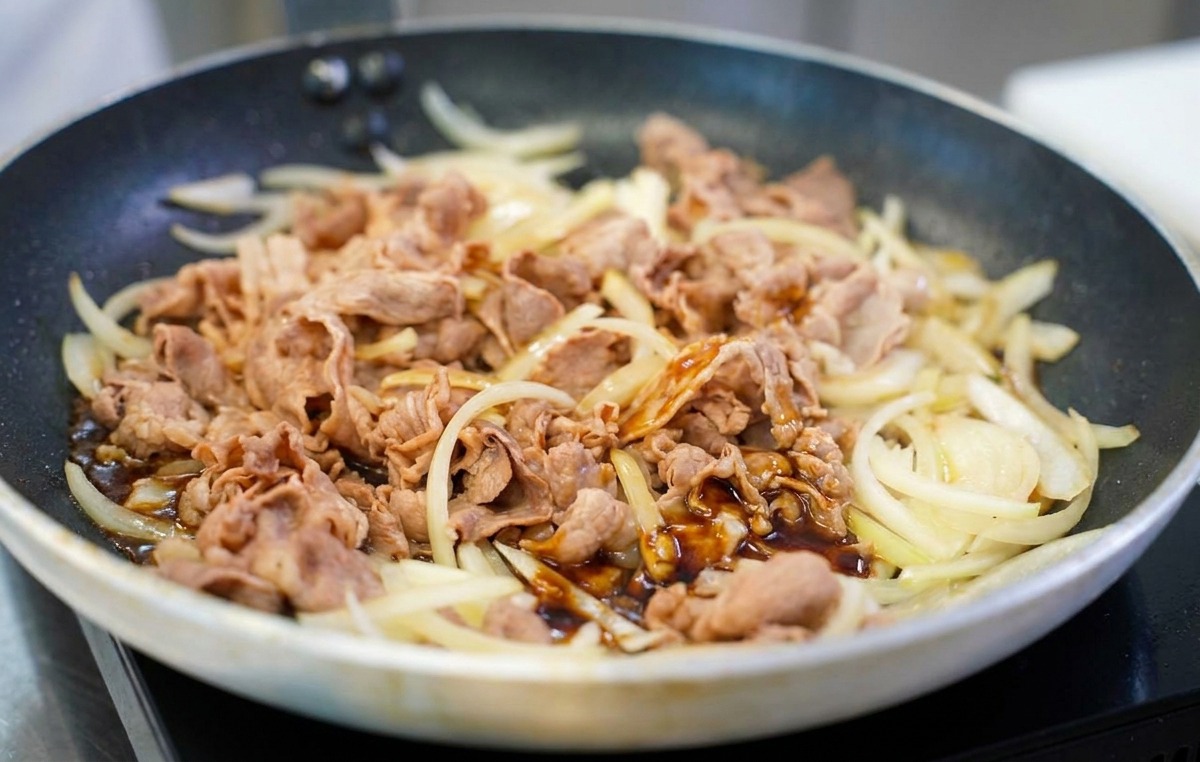 Une sauce savoureuse dun brun foncé et brillant versée sur un mélange de bœuf et doignons sautés dans une poêle.