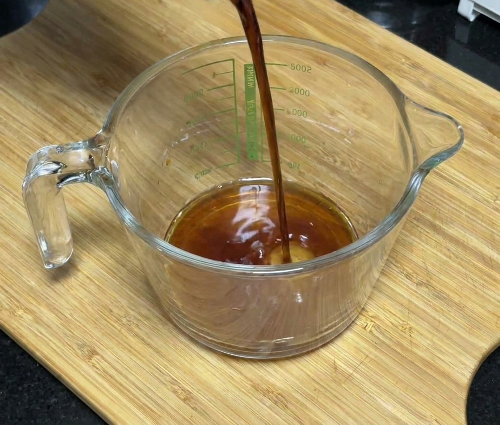 De la sauce soja foncée versée dans un verre doseur contenant du miel et des assaisonnements.