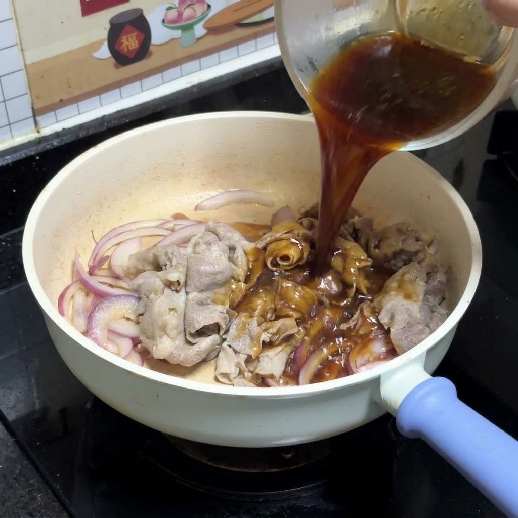 De la sauce teriyaki foncée versée depuis un bol en verre transparent sur les oignons rouges sautés et les tranches de bœuf dans une poêle blanche.