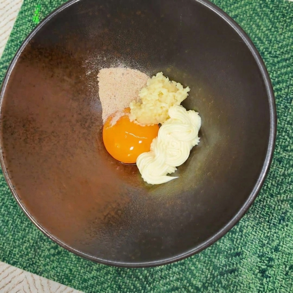 Poudre dassaisonnement versée sur un jaune dœuf et de la mayonnaise dans un bol sombre.
