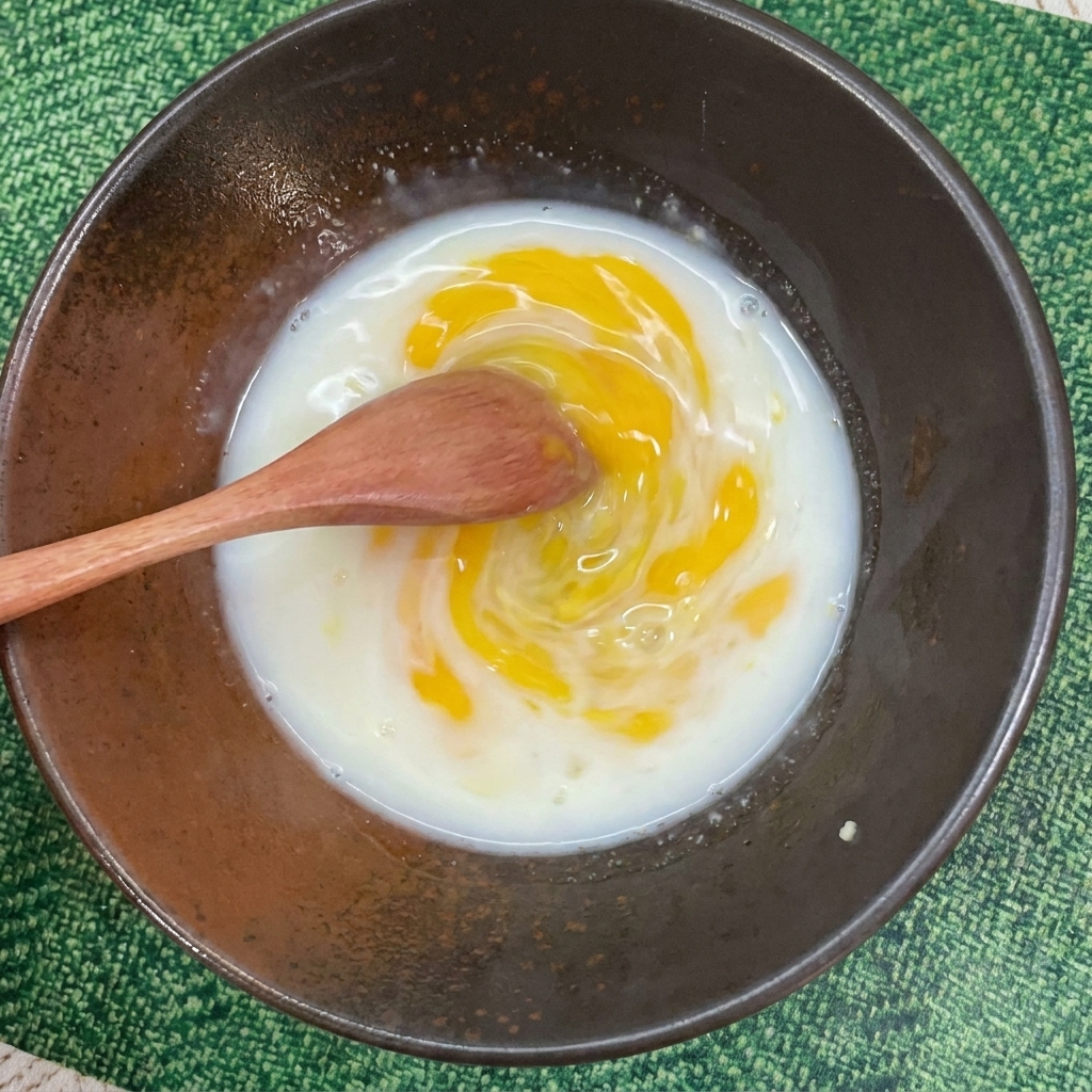 Une cuillère mélangeant un bouillon jaune laiteux dans un bol en céramique sombre.