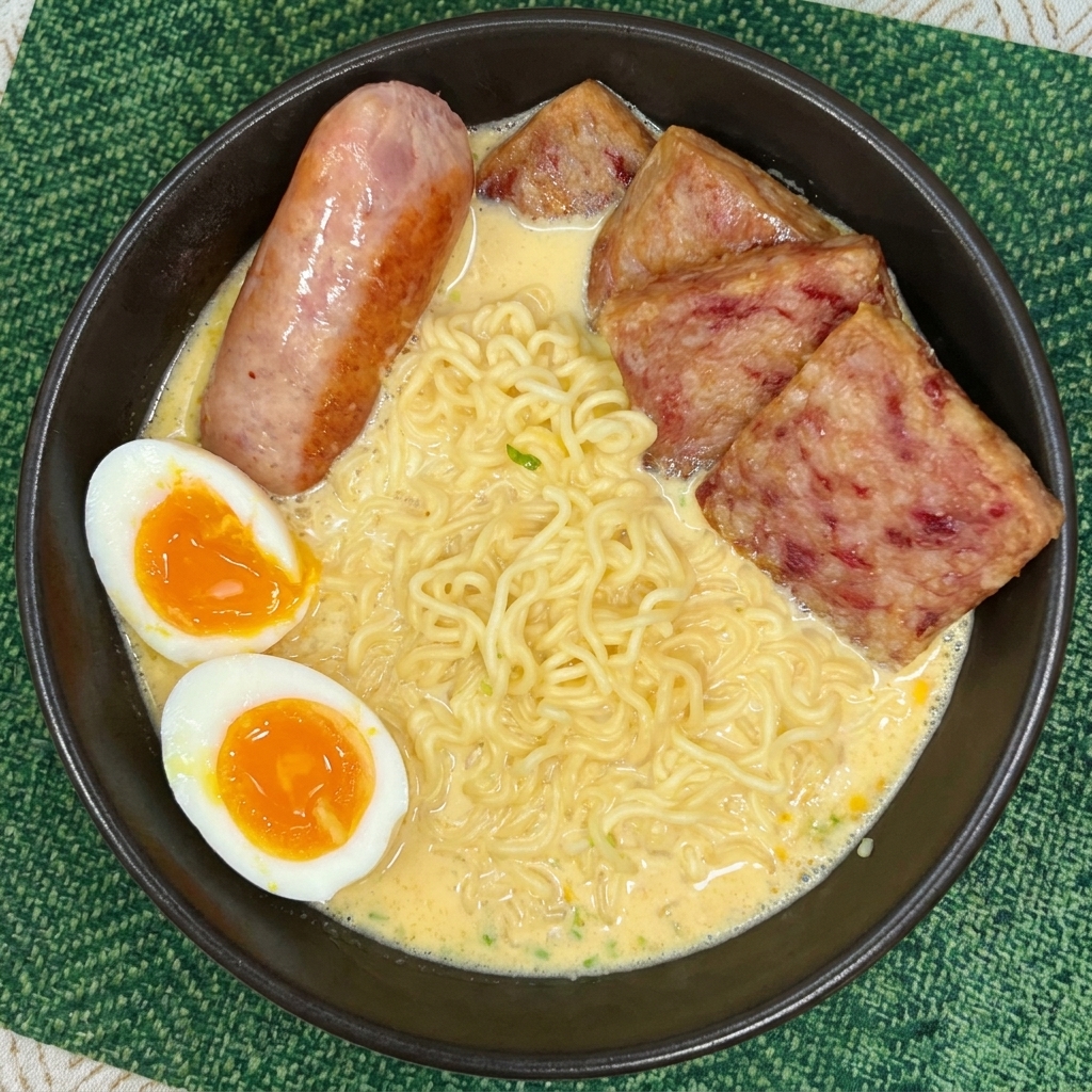 Un bol de ramen garni de tranches de spam, dune saucisse et de deux moitiés dœuf mollet au jaune coulant.