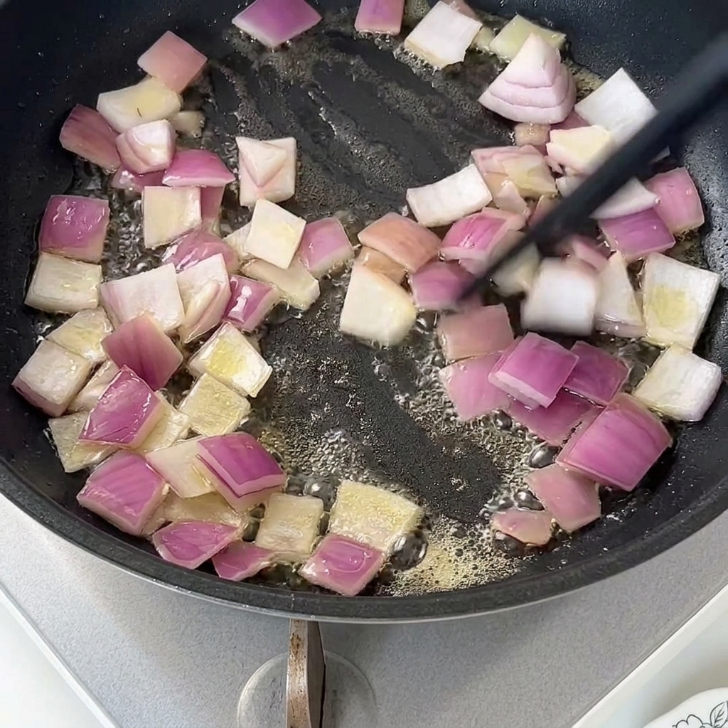 Dés doignons rouges sautant dans le beurre fondu dans une poêle antiadhésive sombre.