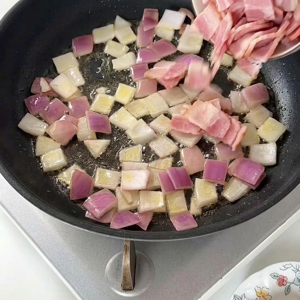 Ajout de morceaux de bacon cru dans une poêle contenant des oignons rouges sautés.