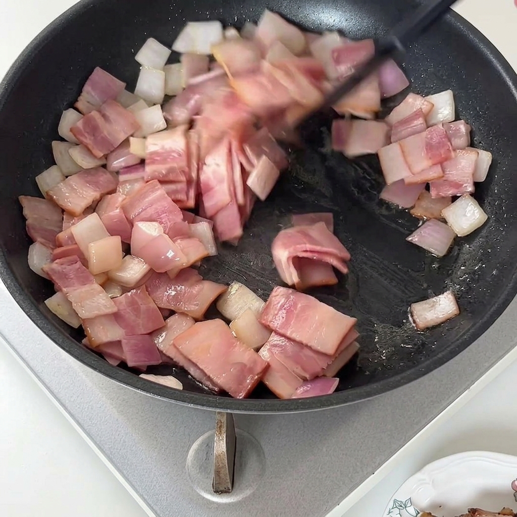 Spatule remuant des morceaux de bacon cuits et des oignons dans une poêle.