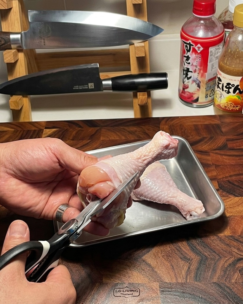 Une paire de ciseaux de cuisine utilisée pour retirer délicatement los dun haut de cuisse de poulet cru sur une planche à découper en bois.