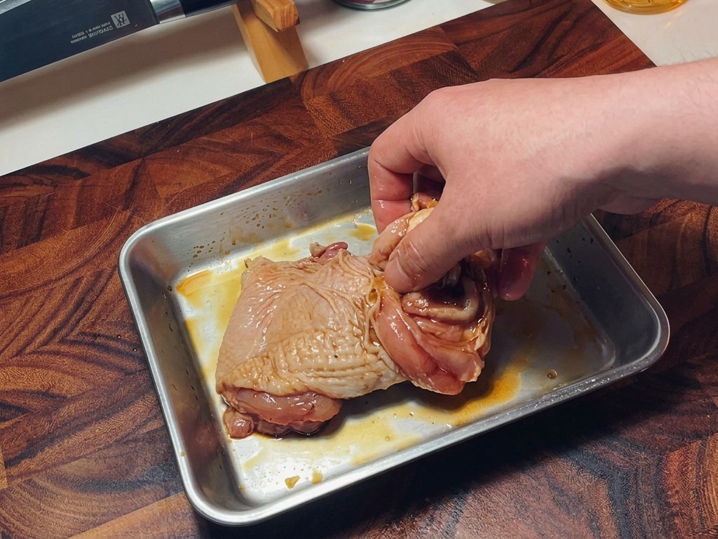 Une main mélangeant des hauts de cuisse de poulet crus assaisonnés dans un plat pour bien répartir la marinade.