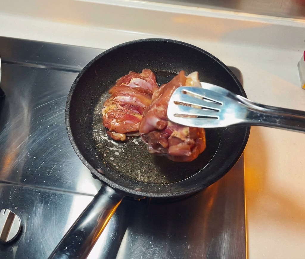 Morceaux de poulet marinés déposés côté peau dans une poêle chaude contenant de lhuile frémissante.