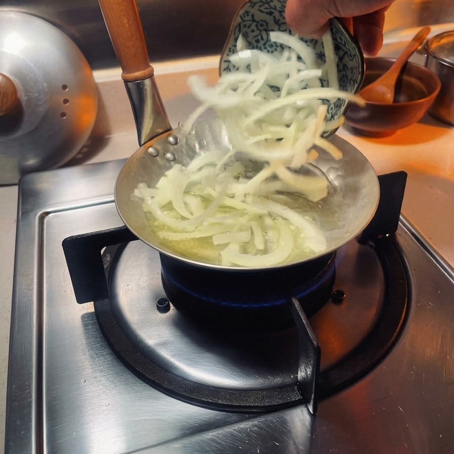 Tranches doignons blancs ajoutées dans une petite poêle spéciale à oyakodon sur un brûleur à gaz.