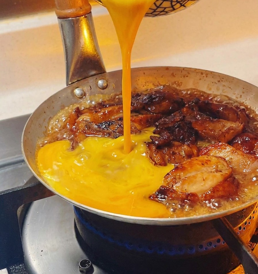 Des œufs battus dun jaune éclatant versés en filet dans une poêle sur des morceaux de poulet frémissants.