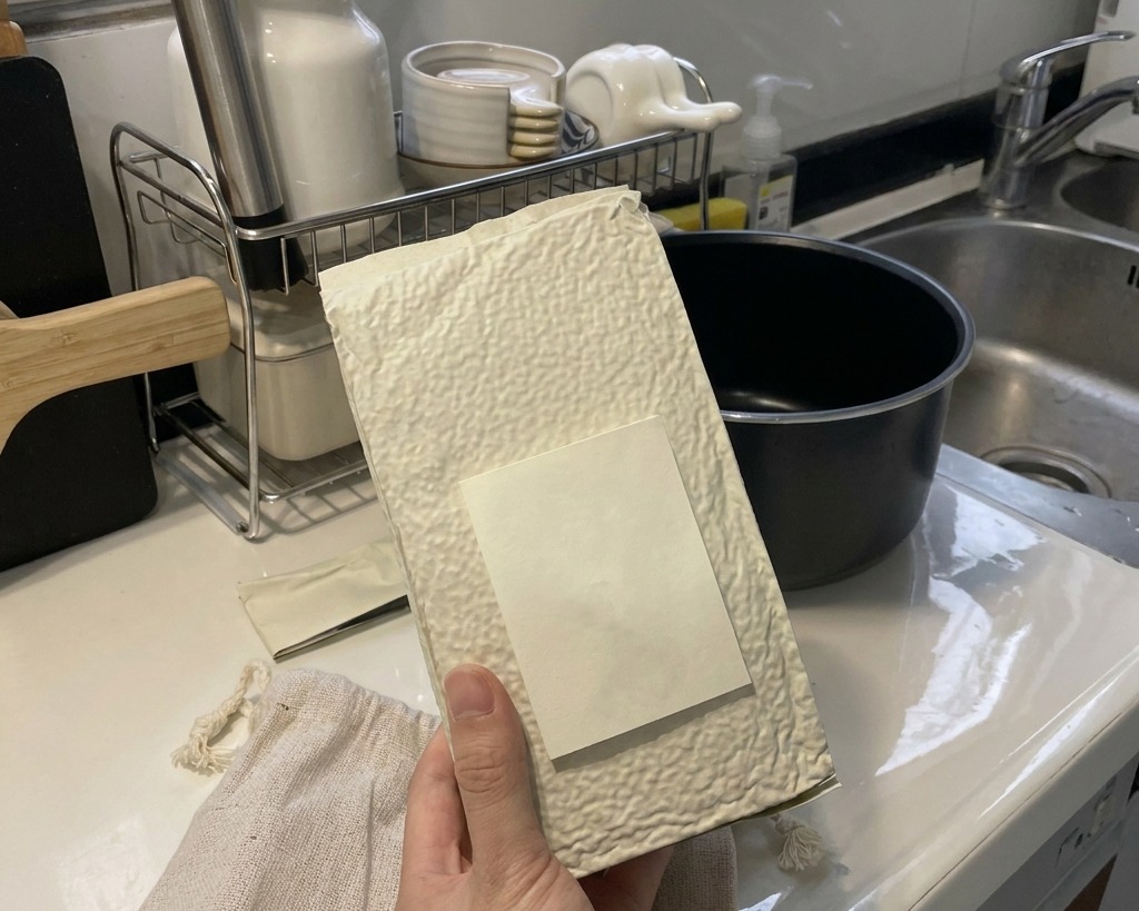 Une main versant du riz blanc à grain court depuis un emballage texturé dans la cuve noire dun cuiseur à riz.