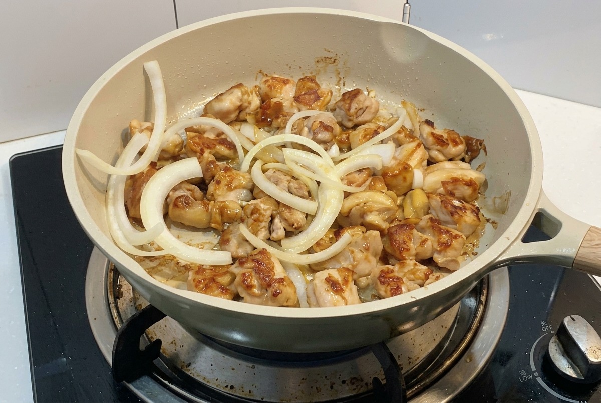 Des lamelles doignon blanc ajoutées dans la poêle où les morceaux de poulet commencent à dorer.
