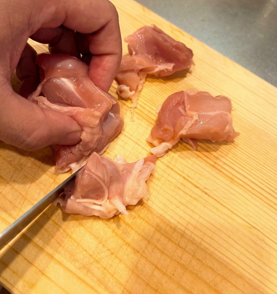 Hauts de cuisse de poulet crus coupés en dés uniformes sur une planche en bois clair.