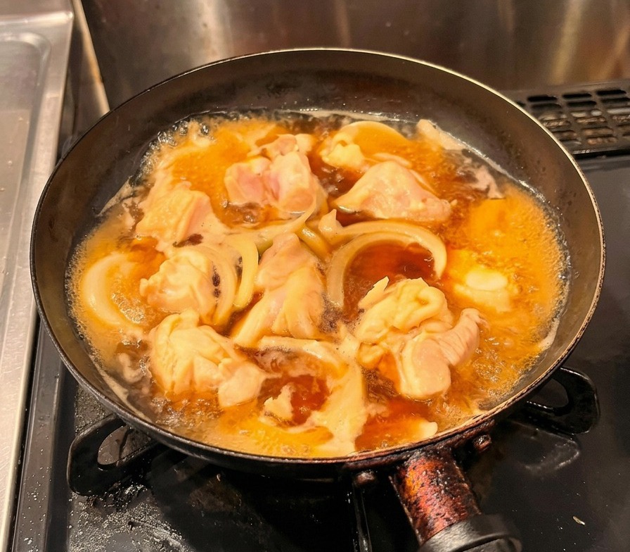Œufs battus jaunes versés en un filet régulier sur le poulet et les oignons mijotant dans une poêle noire.