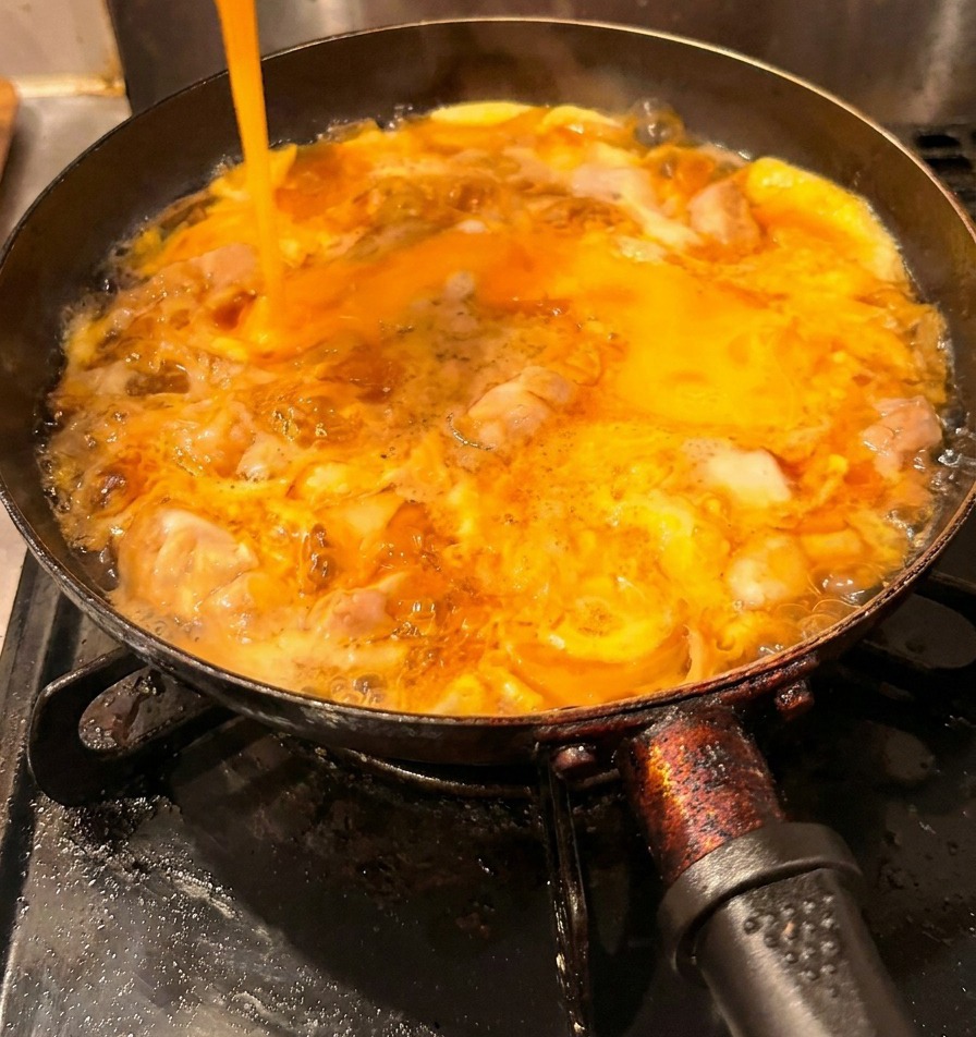 Un filet dœufs battus jaune vif versé dans une poêle sur le poulet et une première couche dœufs cuits.