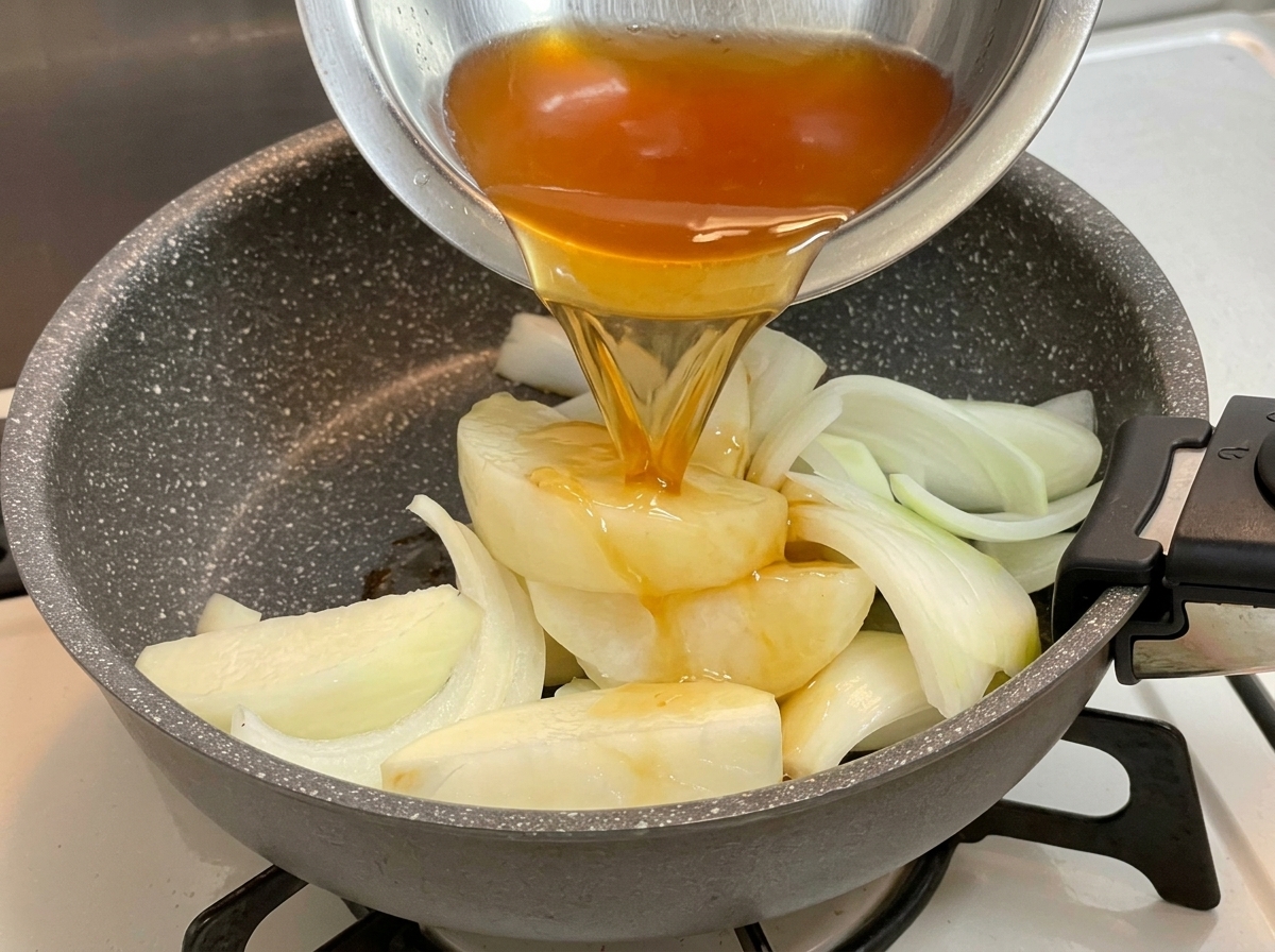 Un liquide dassaisonnement foncé versé depuis un bol en métal sur un lit doignons émincés dans une poêle.