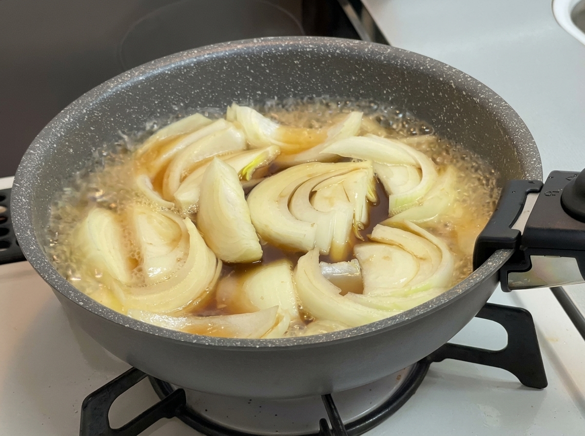 Des oignons mijotant dans un bouillon marron foncé frémissant à lintérieur dune poêle grise sur une cuisinière.