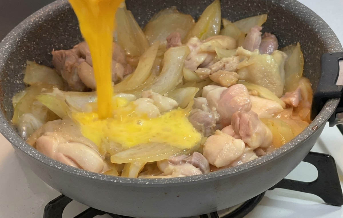 De lœuf battu versé depuis un petit bol sur du poulet et des oignons mijotant dans une sauce.
