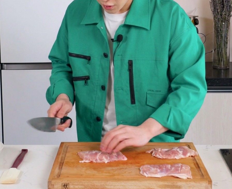 Un couteau pratiquant de légères incisions dans la chair de hauts de cuisse de poulet désossés sur une planche à découper.