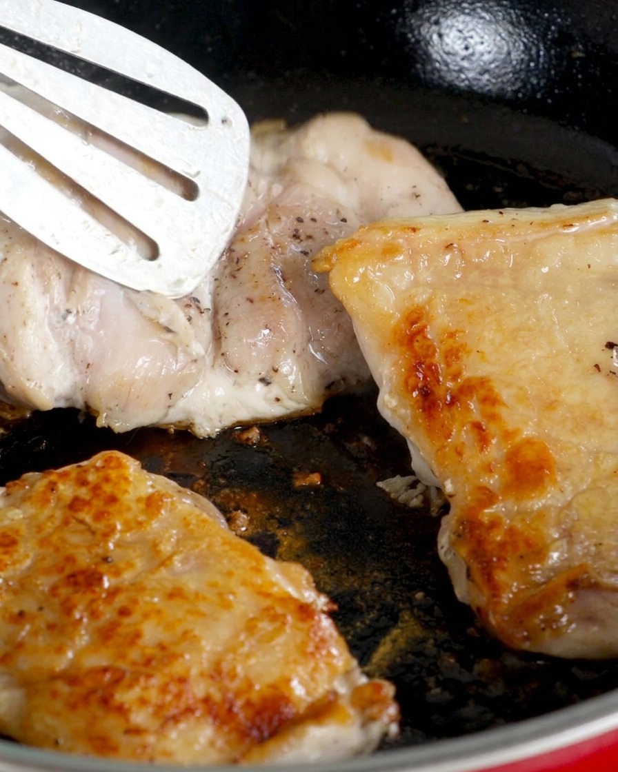 Les hauts de cuisse de poulet retournés dans la poêle, côté peau croustillante vers le haut, pendant que la chair cuit.