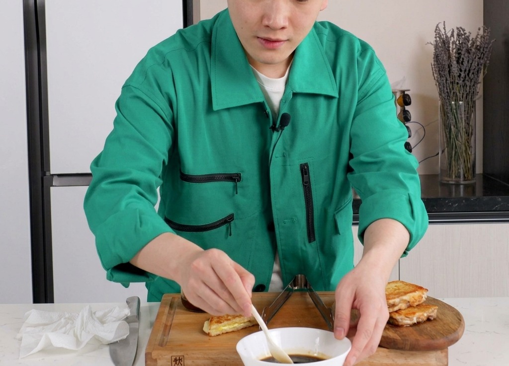 Une personne mélangeant une sauce brune à base de soja dans un bol en céramique blanc avec une petite cuillère blanche.