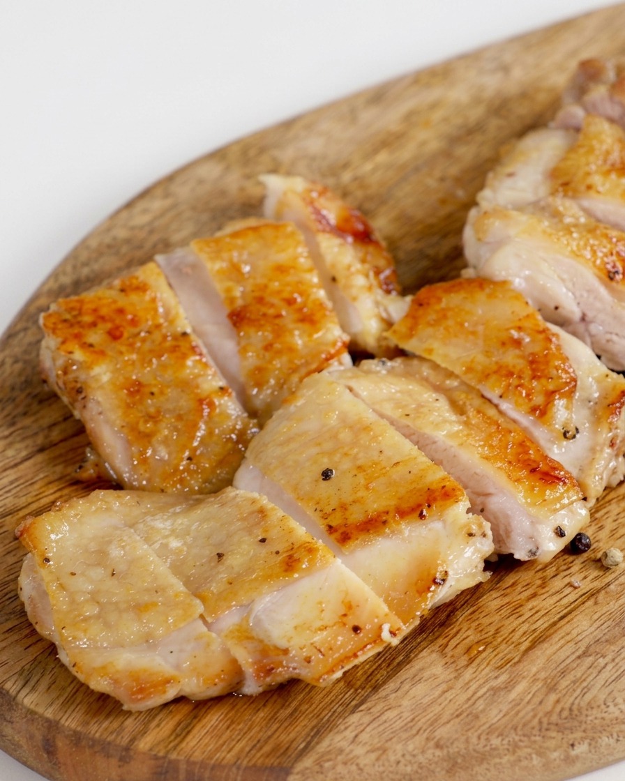 Un haut de cuisse de poulet doré et poêlé, coupé en plusieurs morceaux uniformes sur une planche en bois.