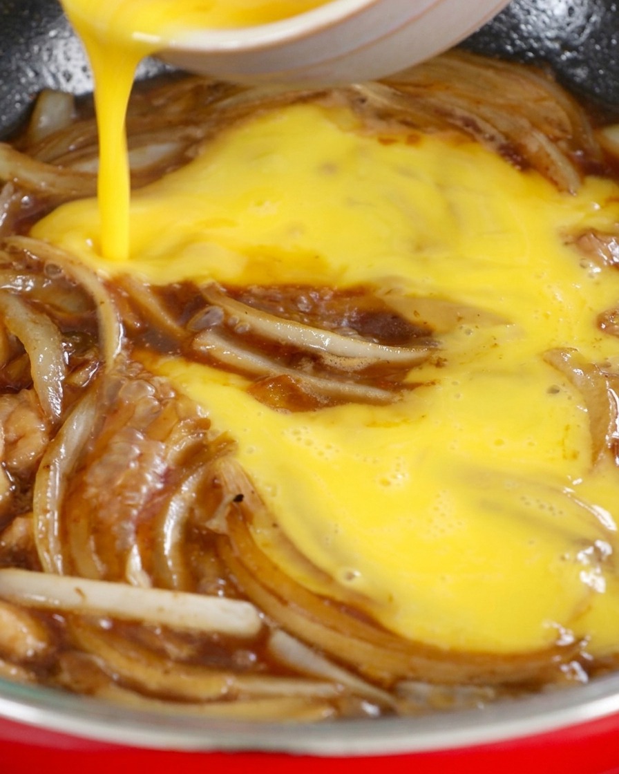 Des oeufs battus versés dun mouvement circulaire dans une poêle remplie doignons émincés et de sauce soja.