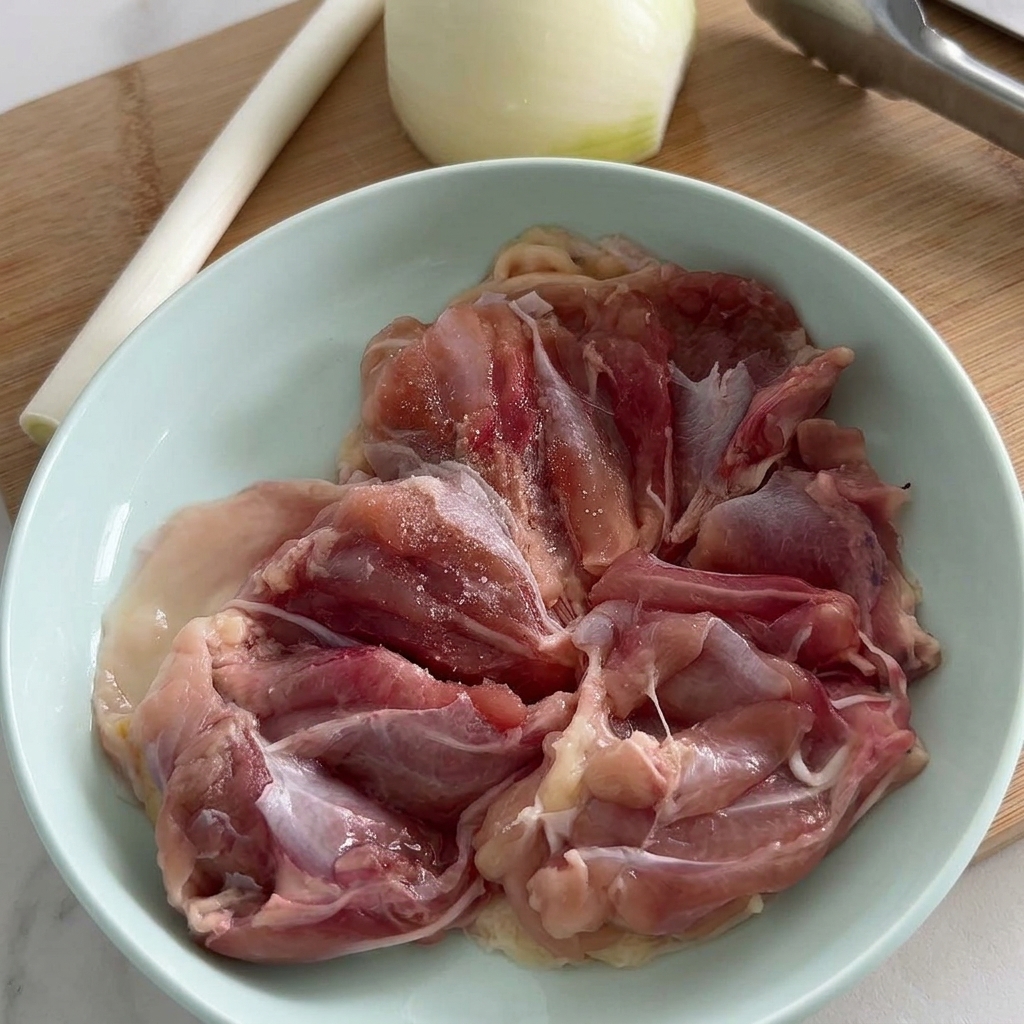 Filets de hauts de cuisse de poulet crus dans un bol bleu clair assaisonnés de sel et de poivre noir fraîchement moulu.