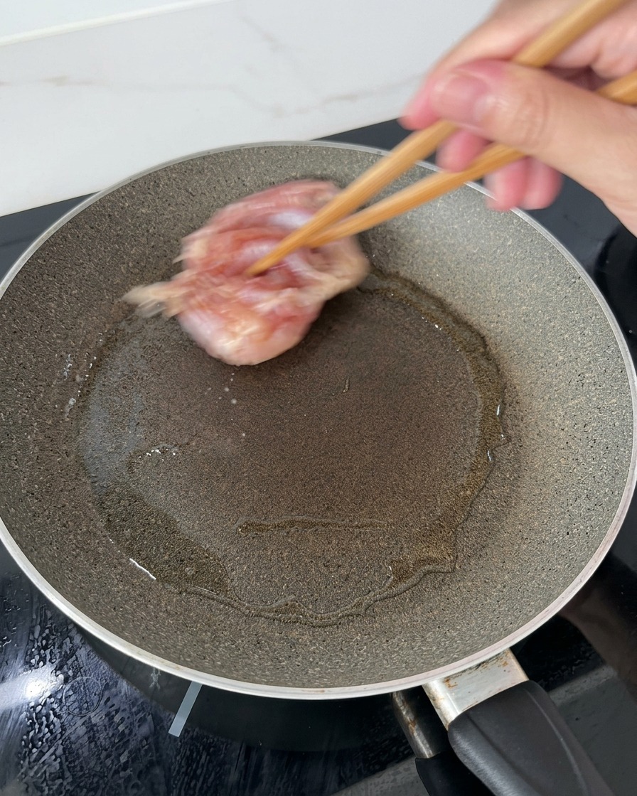 Hauts de cuisse de poulet déposés à laide de baguettes en bois dans une poêle chaude et huilée, côté peau vers le bas.