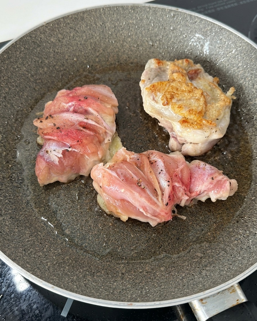 Trois morceaux de hauts de cuisse de poulet dans une poêle, dont un retourné montrant une surface bien dorée et croustillante.