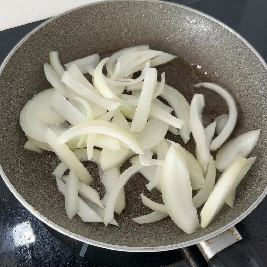 Fines lamelles doignon blanc sautées dans une poêle sombre avec le gras de cuisson résiduel jusquà ce quelles deviennent tendres.
