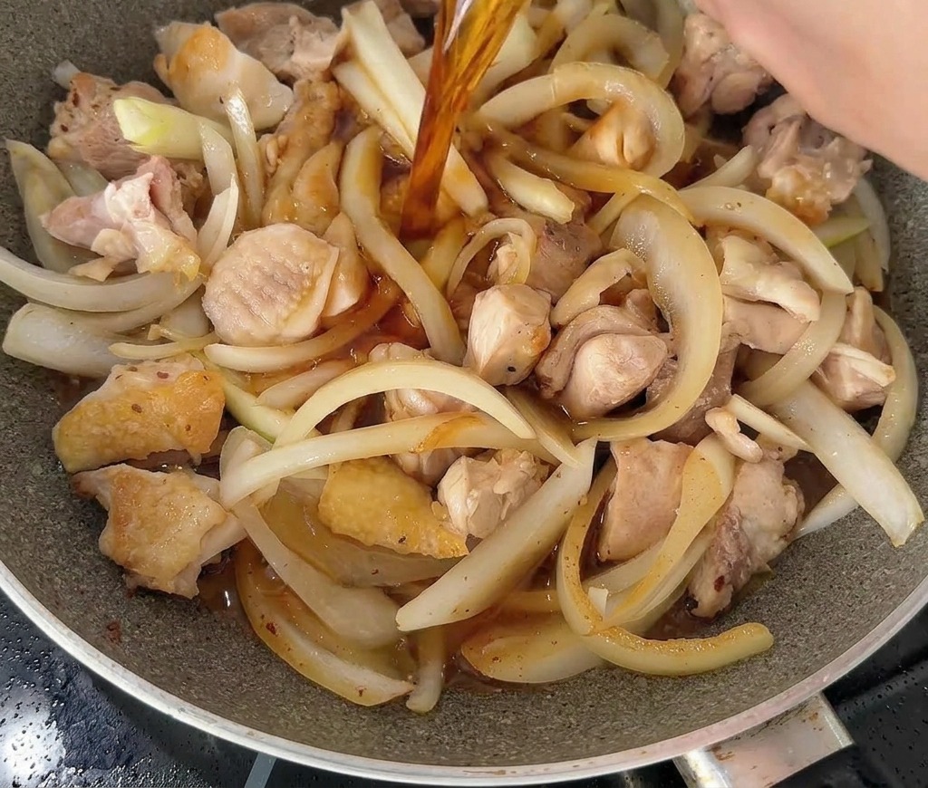 Un liquide sombre et savoureux versé dun bol blanc dans une poêle garnie de morceaux de poulet et de lamelles doignons.