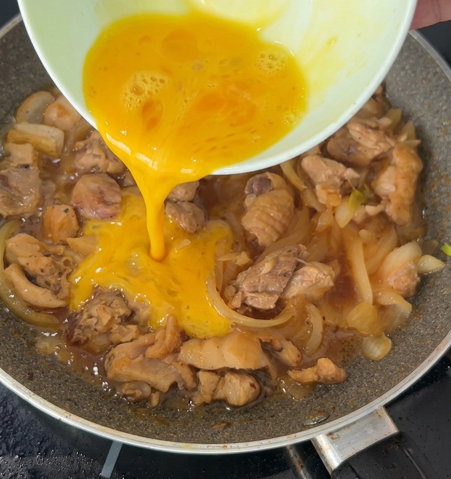 Un filet dœuf battu versé sur le poulet et les oignons frémissants dans une poêle.