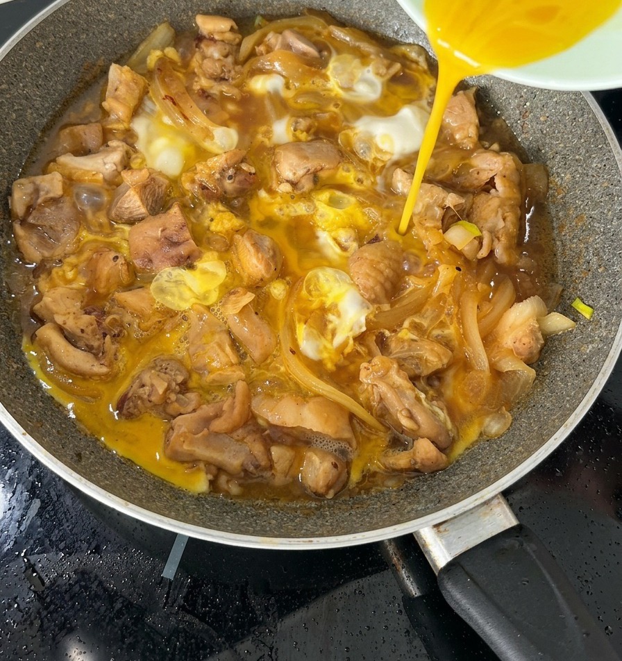 La seconde moitié du mélange dœufs battus versée sur un oyakodon presque terminé dans une poêle.