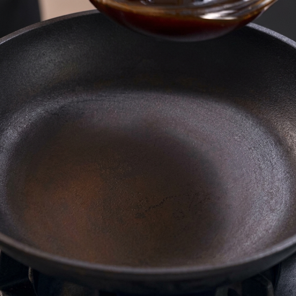 Une sauce oyakodon sombre et sucrée-salée versée dans une poêle noire bien chaude sur la cuisinière.