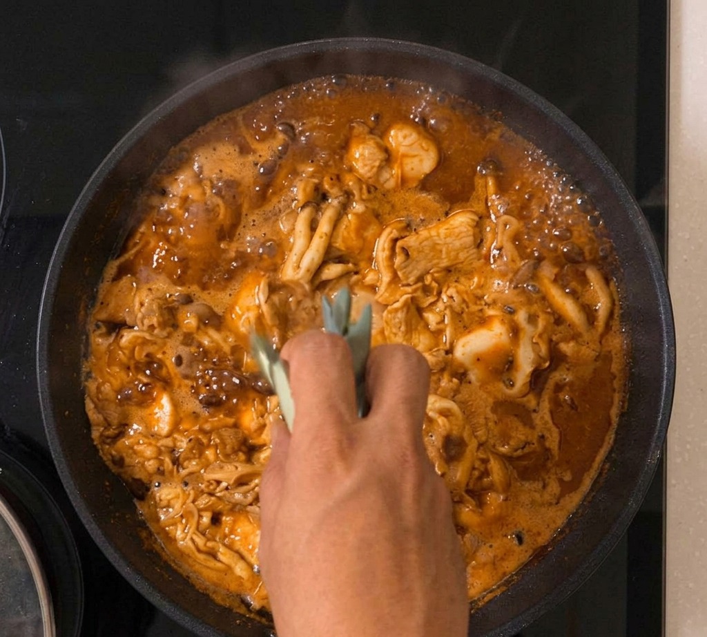 Le mélange oyakodon qui mijote dans une poêle avec des oignons verts visibles au milieu de lœuf et du poulet.