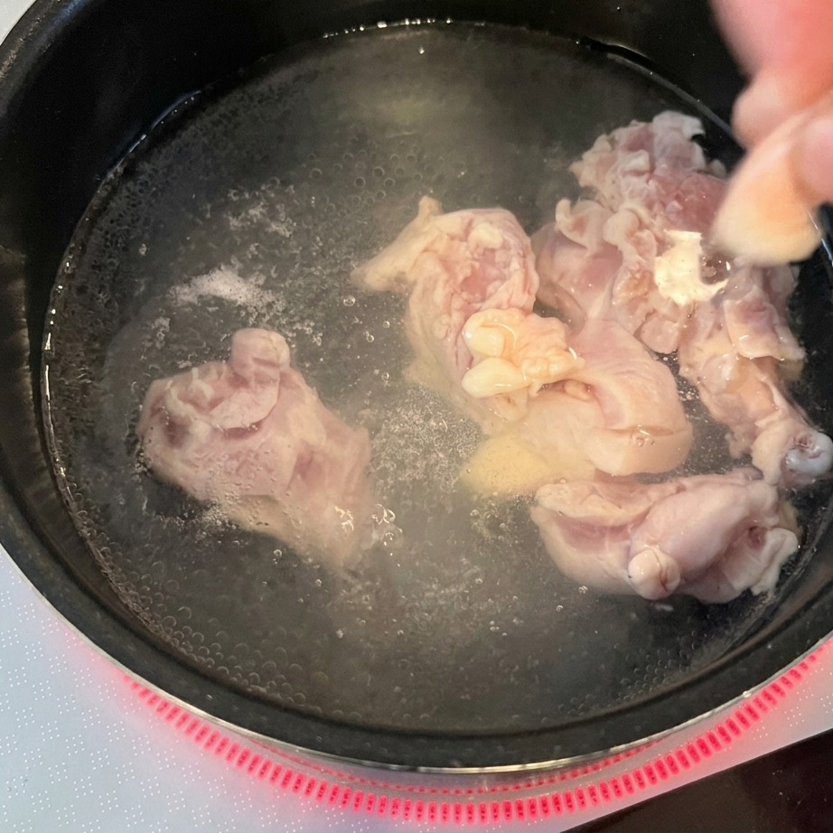 Une personne plonge les morceaux de poulet cru dans une casserole deau bouillante.