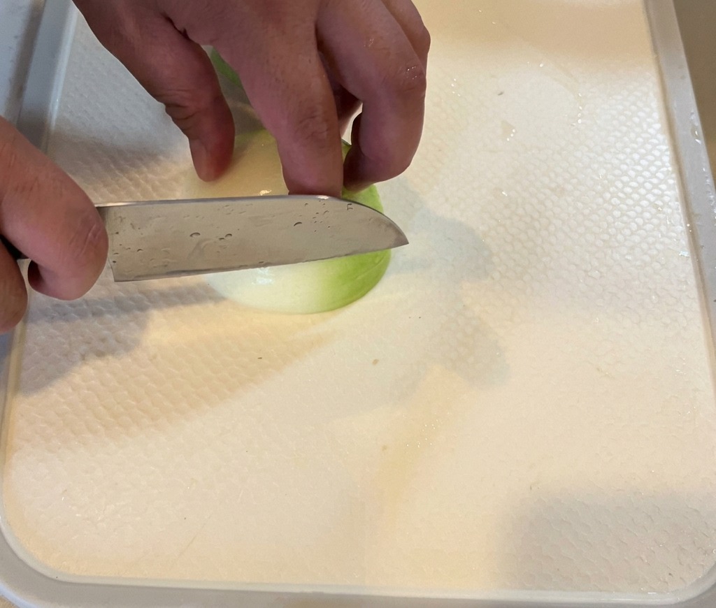 Une personne émince un oignon blanc en fines lamelles sur une planche blanche.