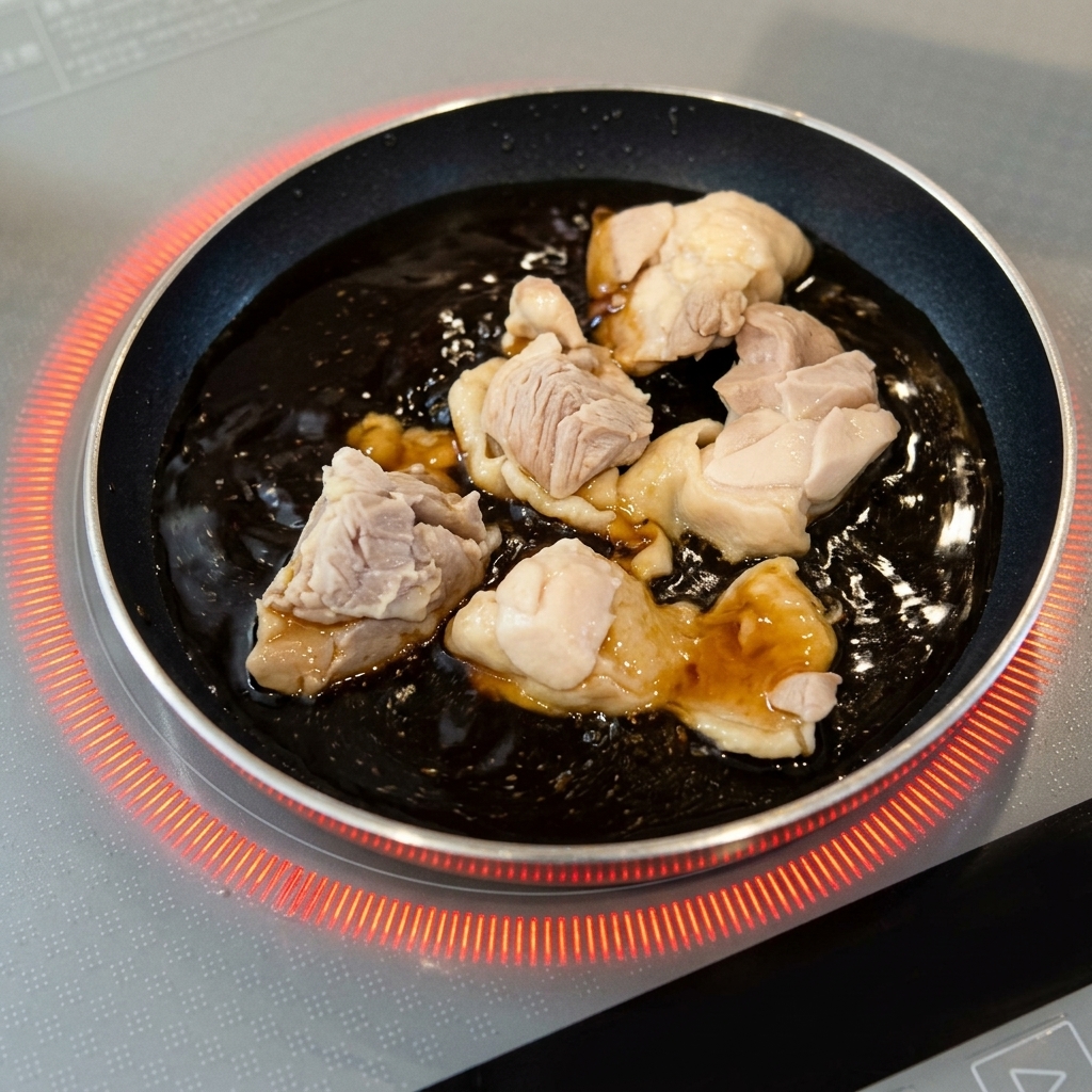 Des morceaux de poulet blanchis mijotent dans une sauce brun foncé bouillonnante dans une petite poêle.