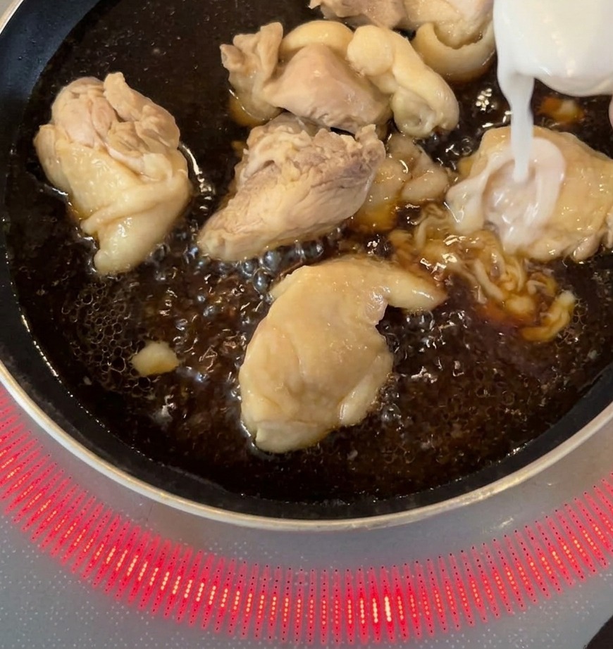 Des lamelles doignon blanc sont ajoutées à la poêle avec le poulet qui mijote dans la sauce foncée.