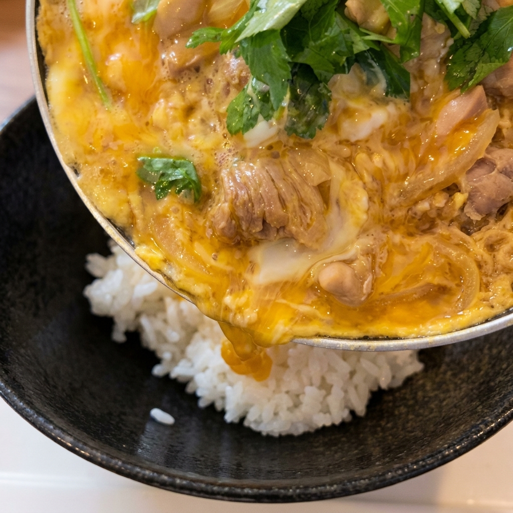 Une poêle est inclinée pour faire glisser la garniture de poulet et dœuf sur un bol de riz blanc fumant.