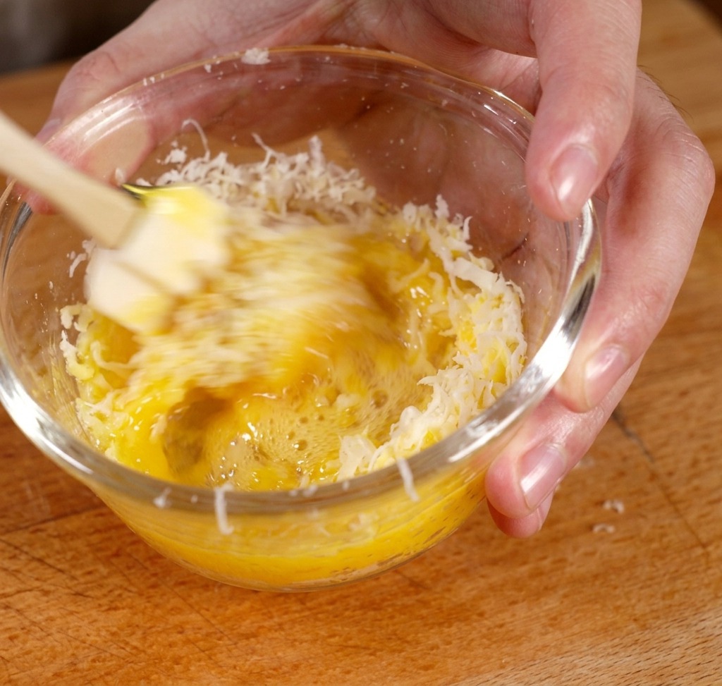 Mélange du jaune dœuf et du fromage râpé dans un bol pour former une pâte jaune épaisse.