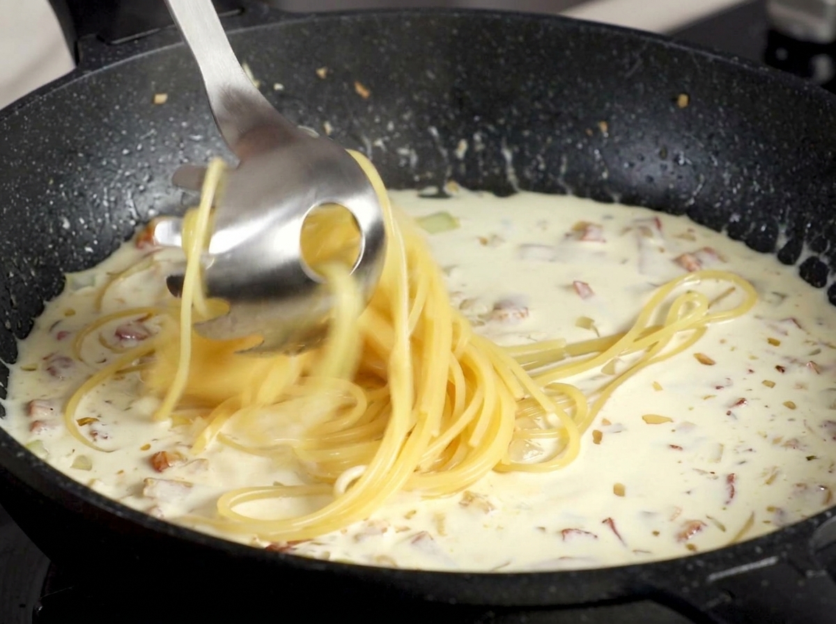 Spaghetti transférés avec une cuillère à pâtes dans une sauce crémeuse aux lardons.
