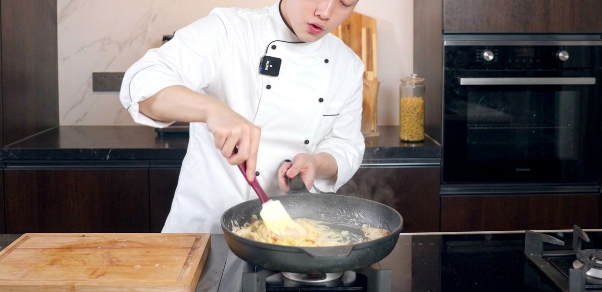 Chef mélangeant les pâtes crémeuses dans une poêle avec une spatule.
