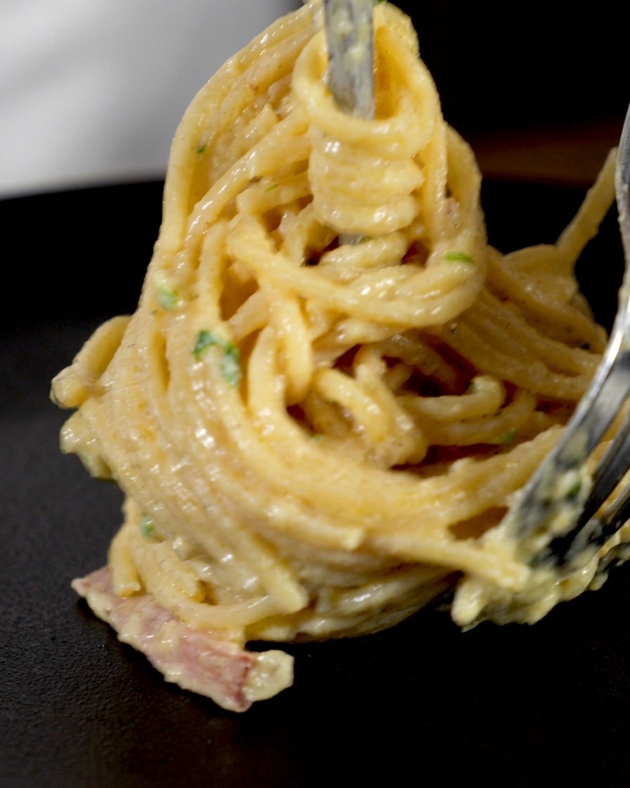 Spaghetti crémeux et morceaux de bacon enroulés serrés autour dune fourchette à découper pour former un nid vertical.