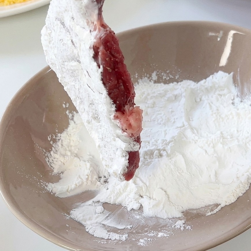 Une côtelette de porc enrobée de farine blanche dans un bol en céramique beige.