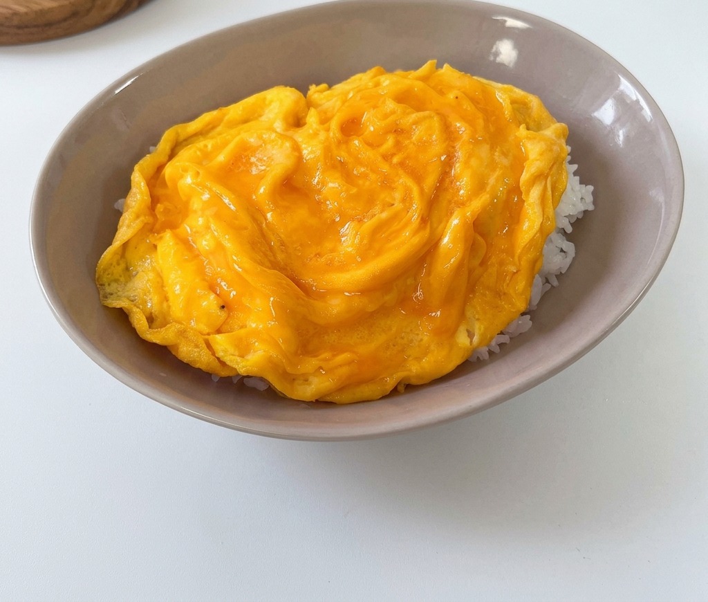 Une omelette jaune, douce et moelleuse, posée sur un lit de riz blanc dans un bol creux gris.