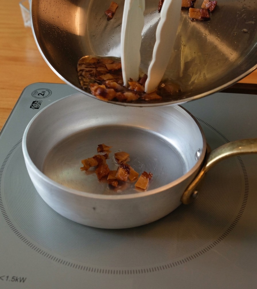 Transfert des morceaux de guanciale dorés et de leur gras fondu de la poêle vers un petit bol.