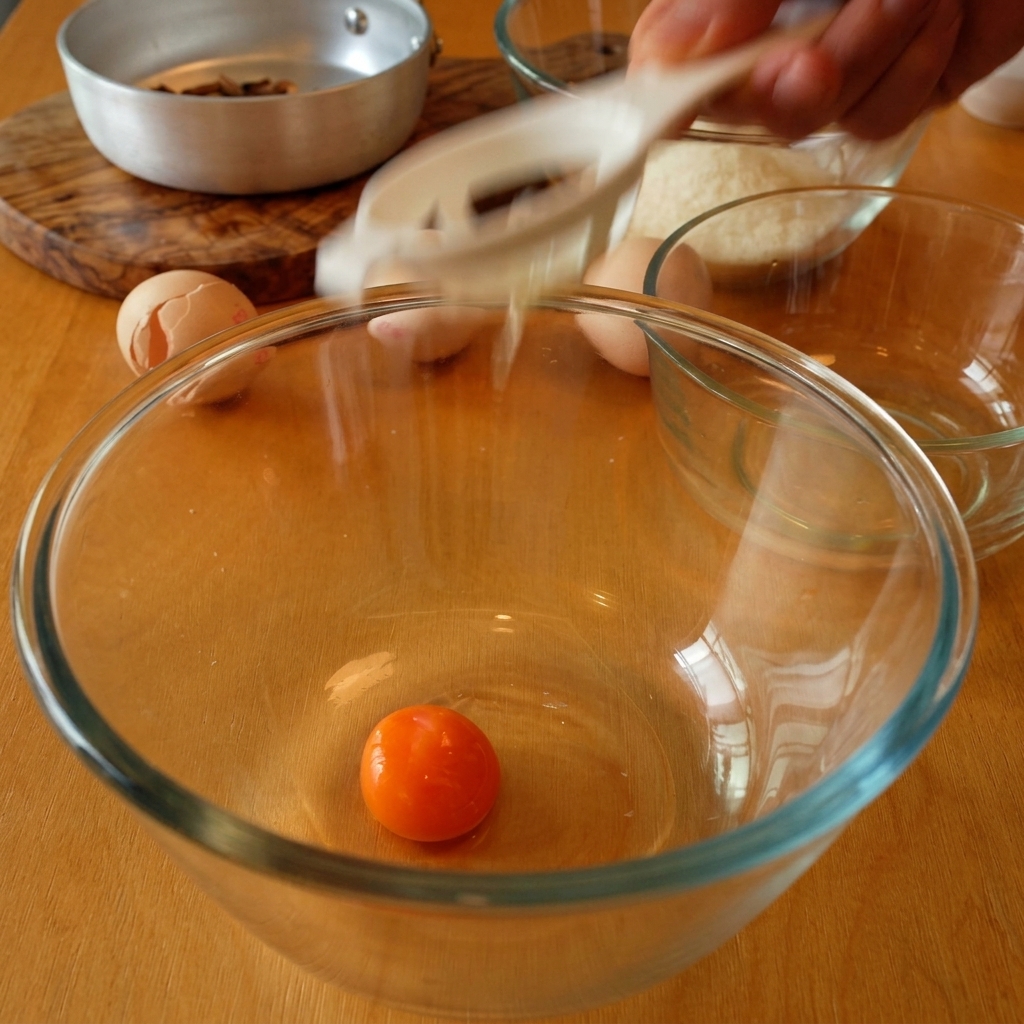 Un jaune dœuf orange vif dans un bol en verre tandis que le blanc sécoule à travers un séparateur.